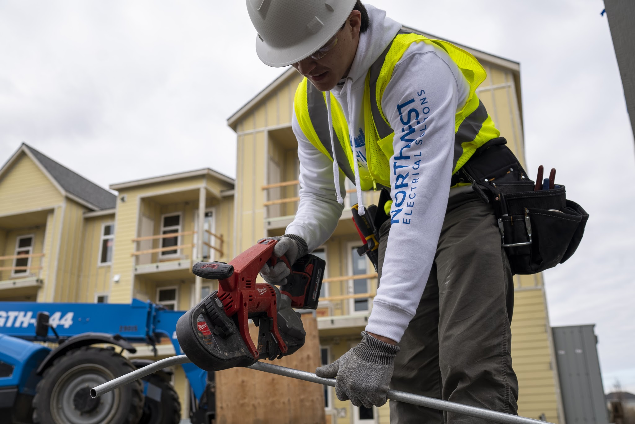 Technician in branded hoodie bending electrical conduit on site