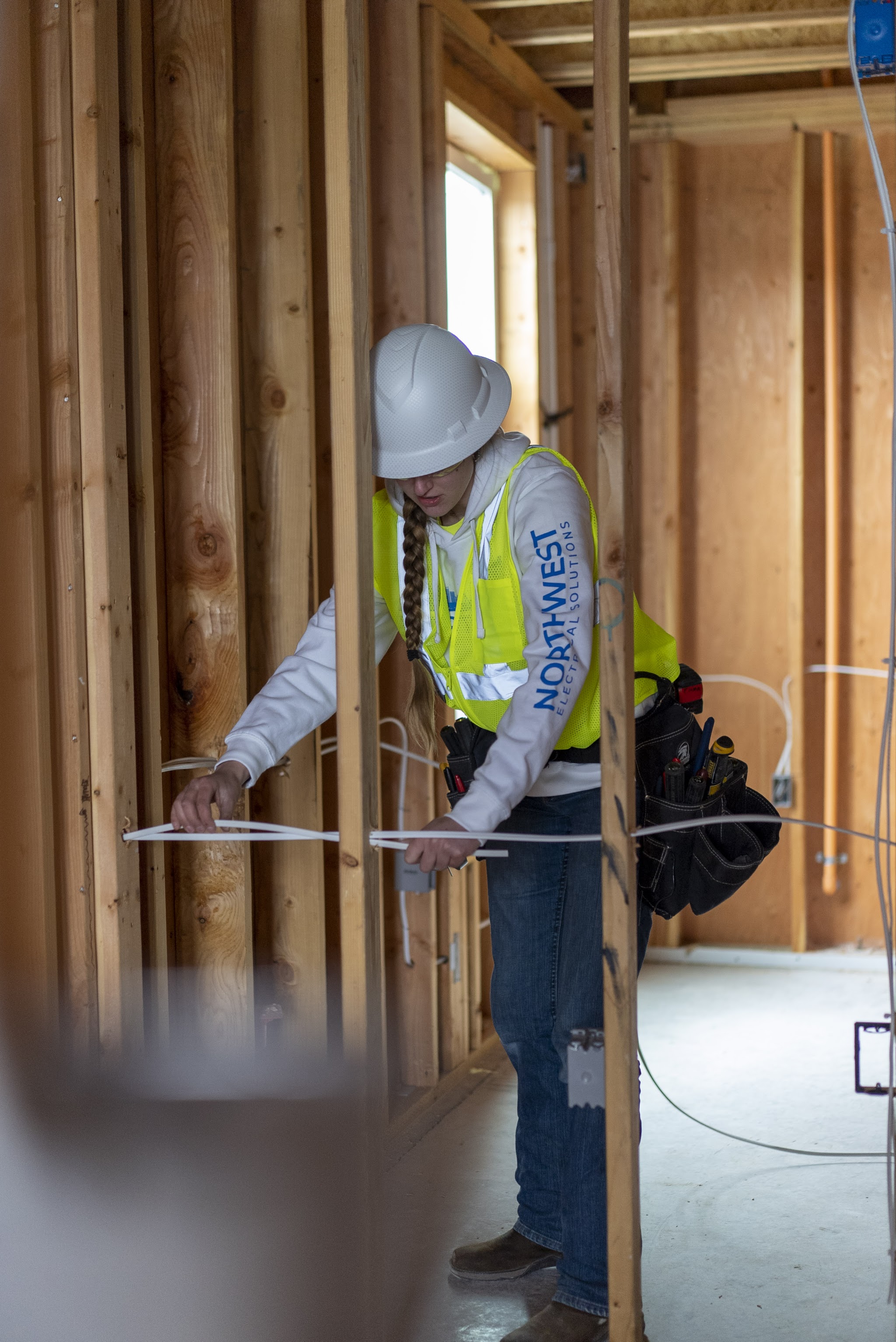 Technician running electrical wire inside stud-framed walls on a new construction site